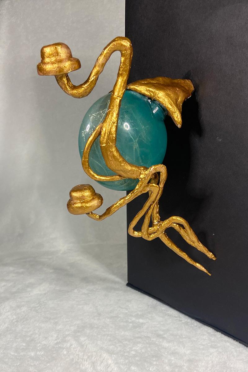 A clay model of a gold hat stand with a green translucent bubble like a fish bowl that can light up when a hat is placed on it. The model is mounted onto a black backdrop.