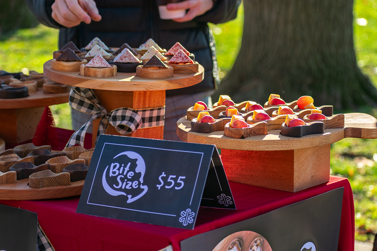 Close-up image of products on a market display table; the product, named “Bite Size,” is a wooden serving tray with several scoop-like components that can hold a small amount of food.