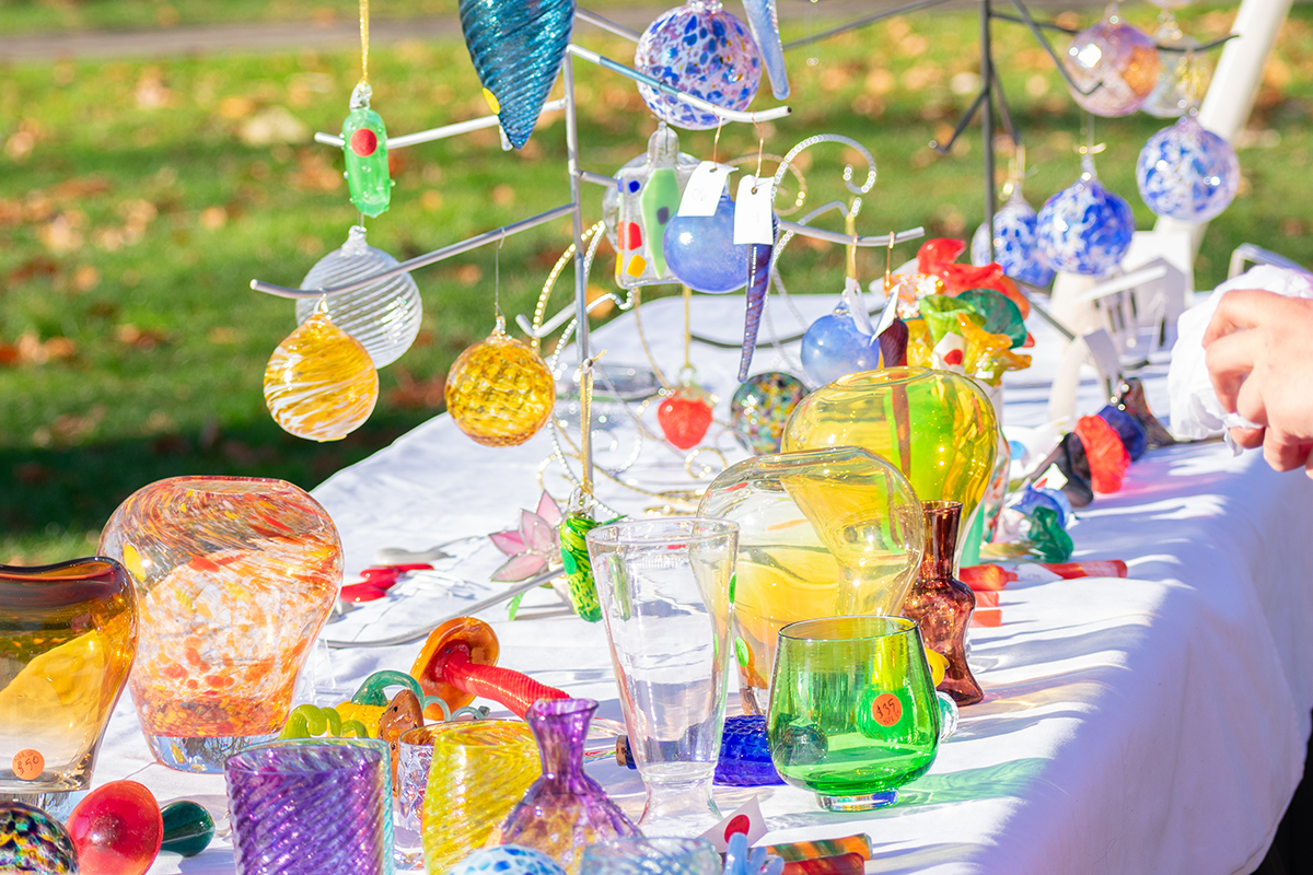 An assortment of colorful, shiny, glass objects with a host of shapes, textures, and proportions, arranged on a market display table.