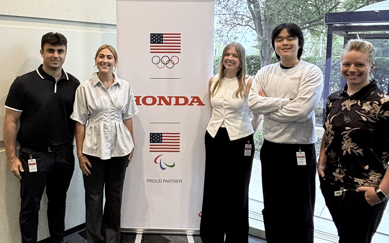 Students posing for a photo in front of a banner at Honda R&D.