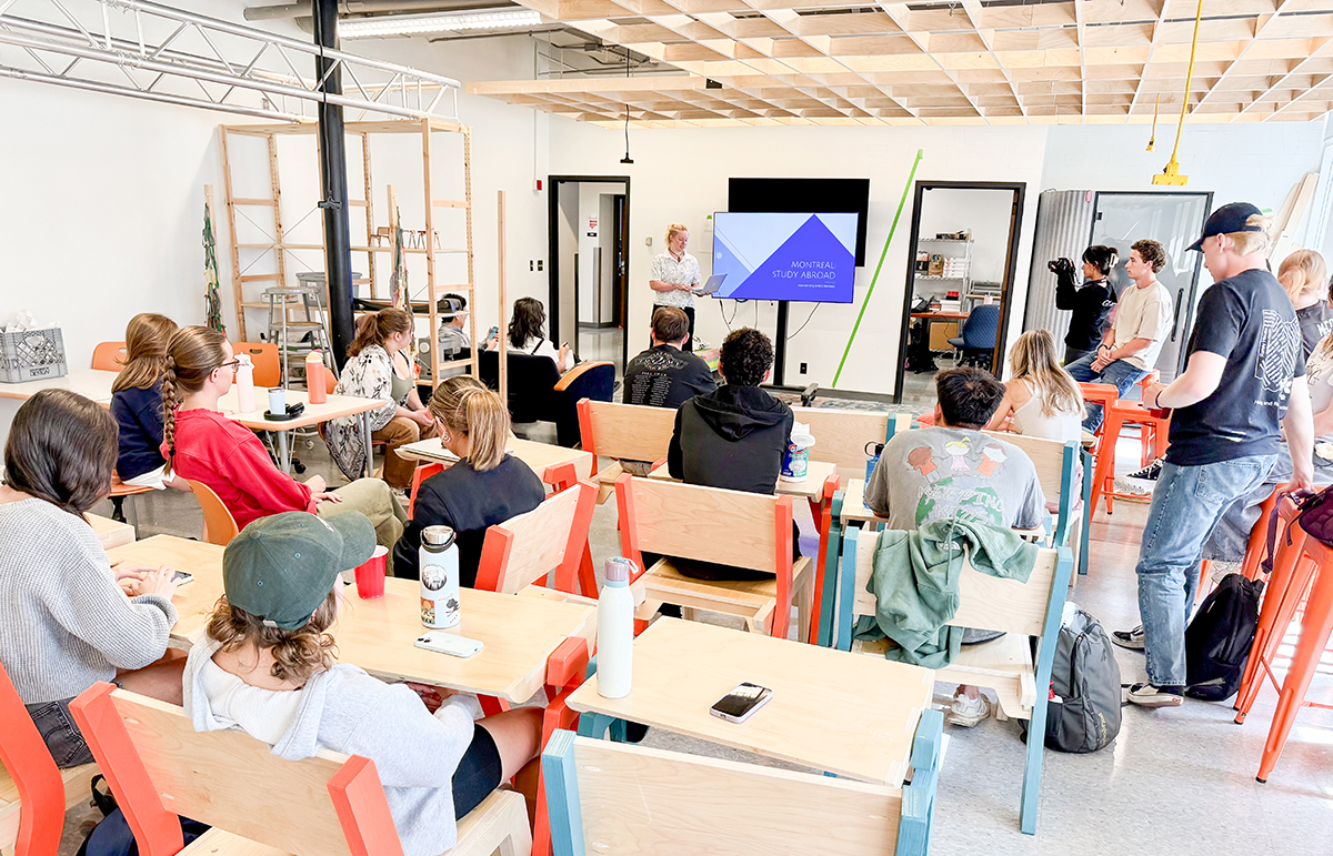 Photo of a student presenting next to a TV in front of a classroom full of students.