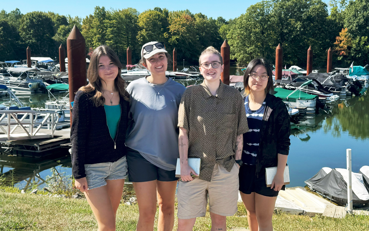 Students posing for a photo in front of a marina filled with boats.