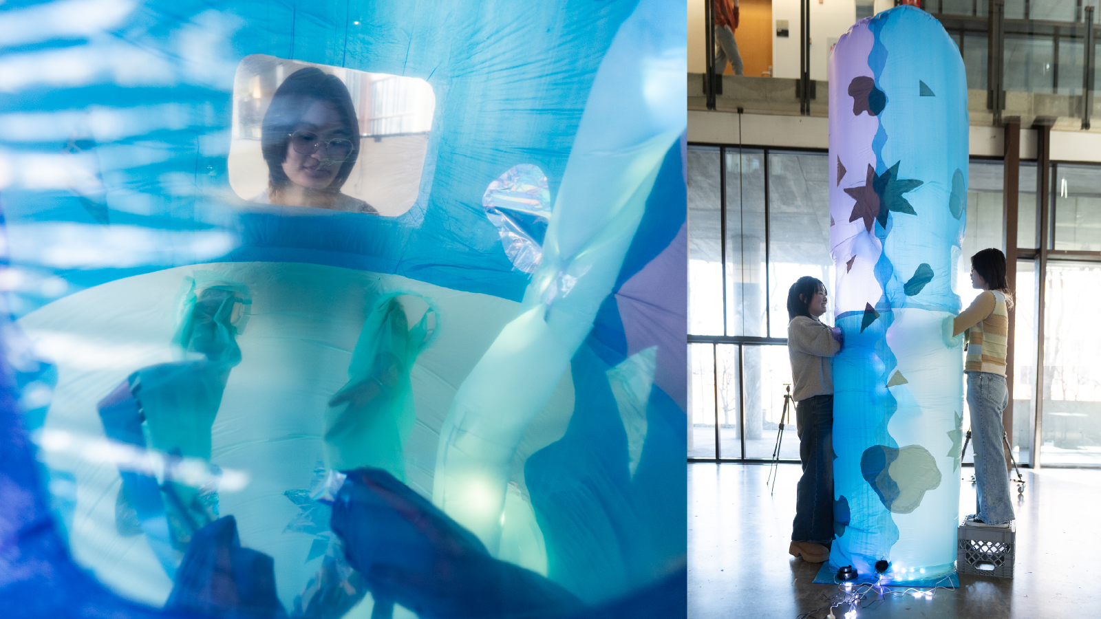 Two people standing on either side of a large, blue and purple inflatable cylinder standing about 11 feet tall. Their arms are inside the inflatable and light is passing through the semi-transparent membrane.