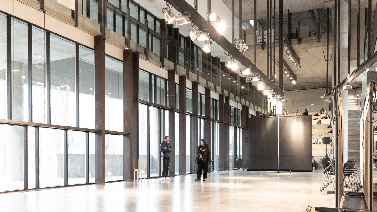 An interior image of Knowlton School of Architecture atrium, with concrete floors and walls. A row of floor-to-ceiling windows line the left.