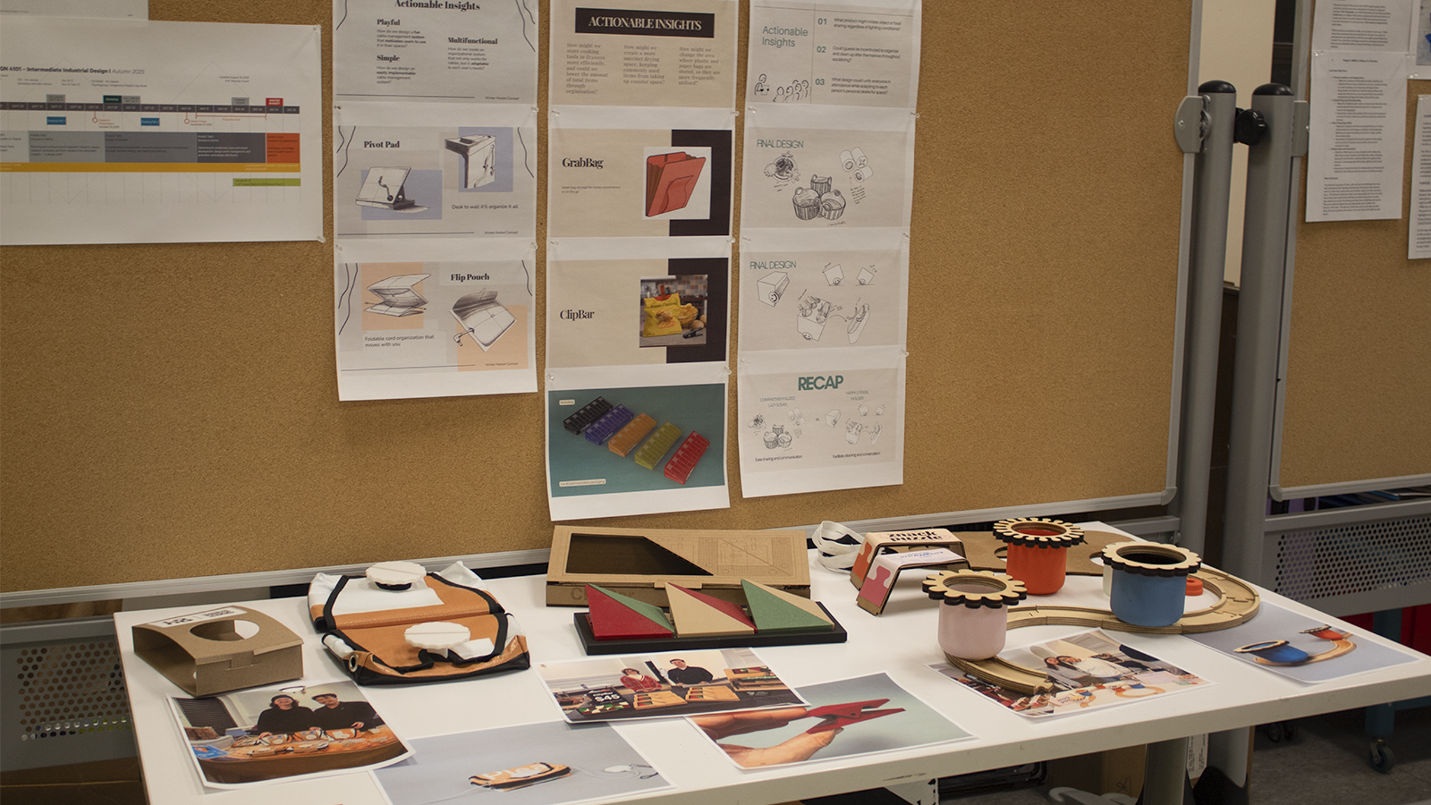 Design project display with sketches, labeled concept boards, and small physical prototypes arranged on a corkboard and table