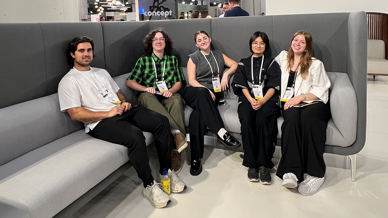 Five smiling design students seated on a large grey sectional with a high back. 