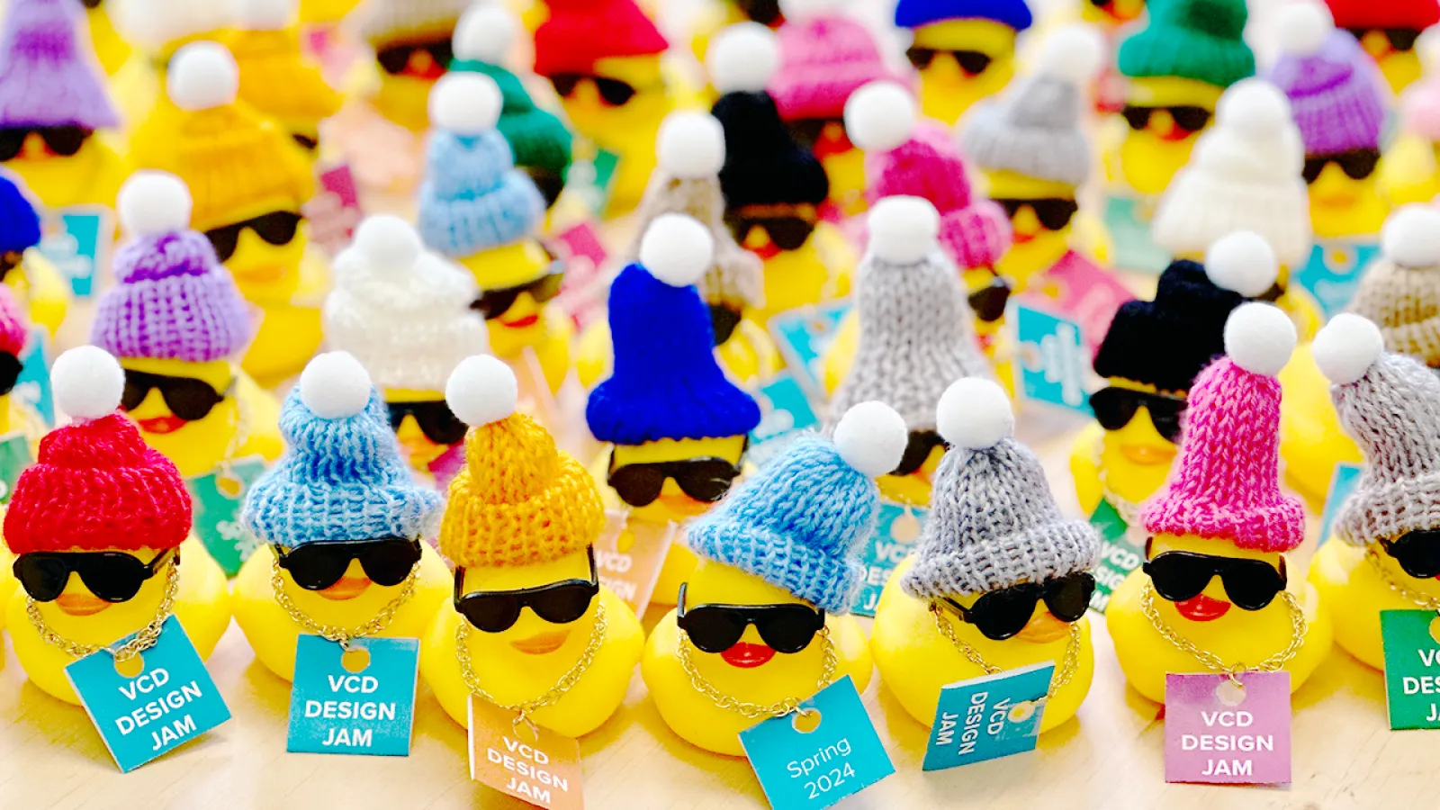 Rubber ducks wearing sun glasses and stocking caps holding signs that say "Visual Communication Design Jam 2024!"