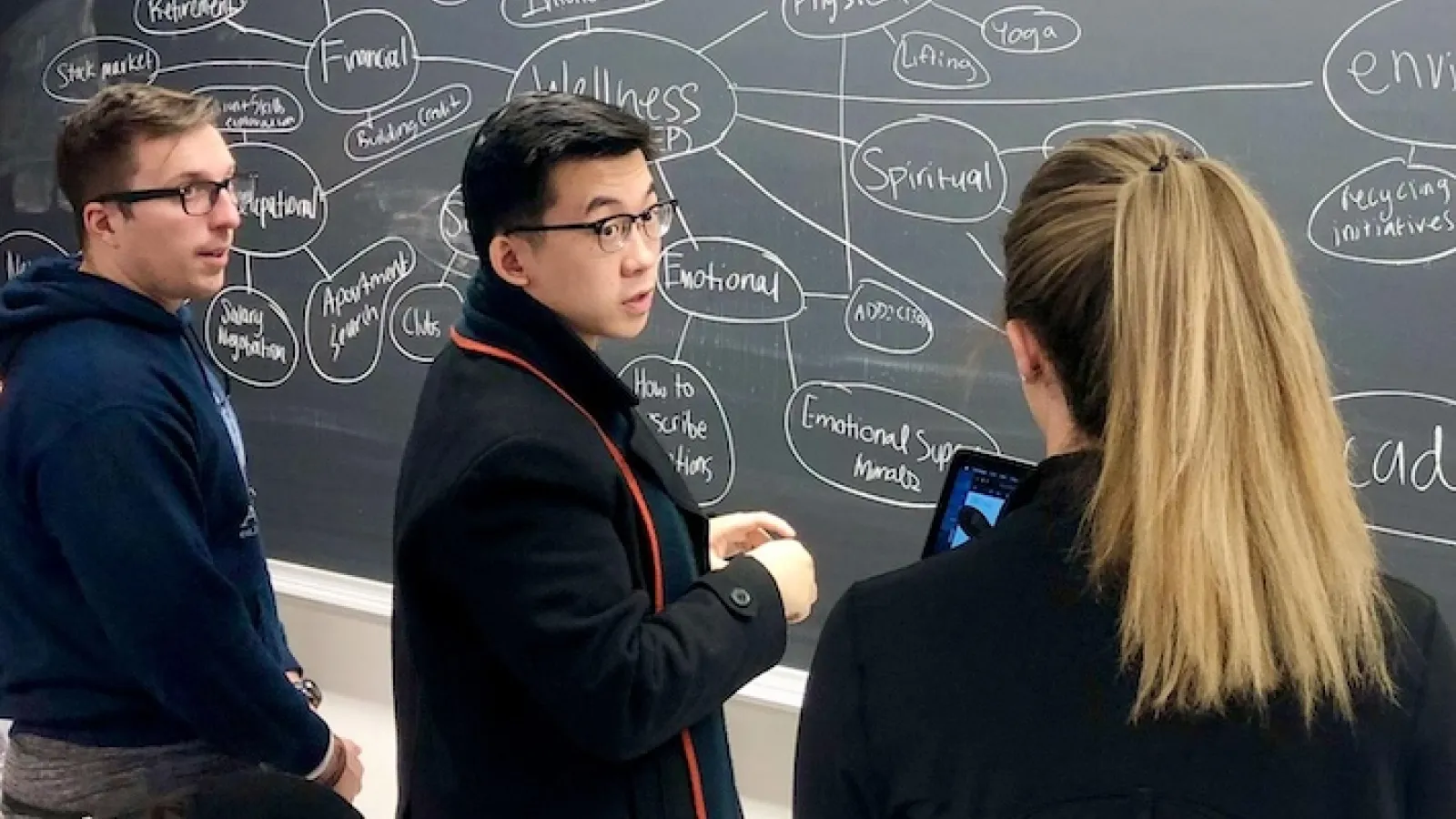 Three students collaborating on a mind map at a chalkboard. 