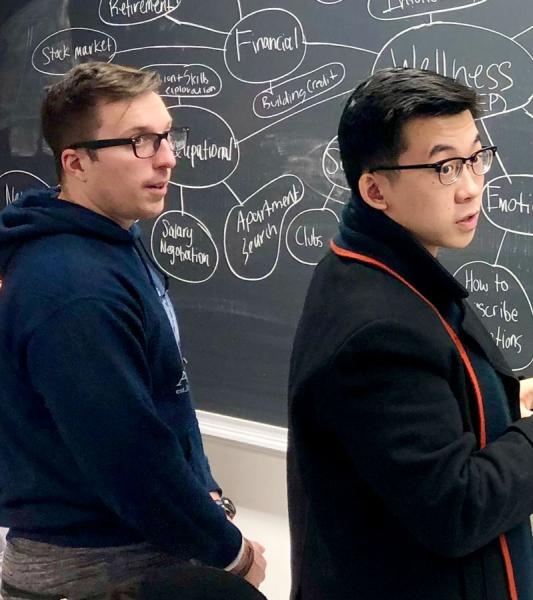 Three students collaborating in front of a chalkboard with a mind map on it.