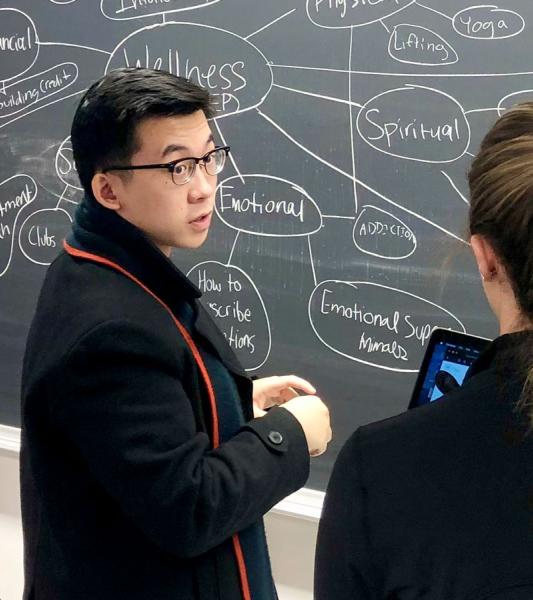 Three students collaborating in front of a chalkboard with a mind map on it.