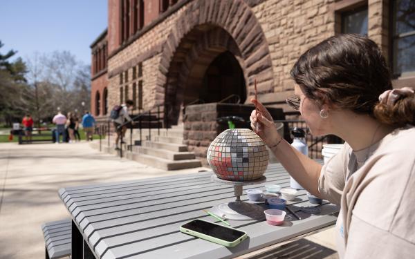 A student paints on an art project outside of Hayes Hall on a warm spring day.