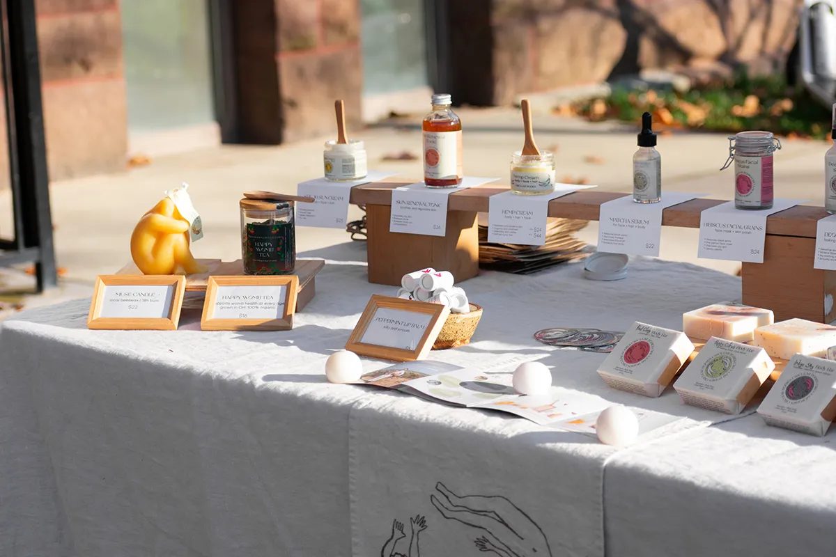 Several self-care products, like soaps, moisturizers, and scented candles, all with natural colors and product information cards, neatly arranged on a market display table.