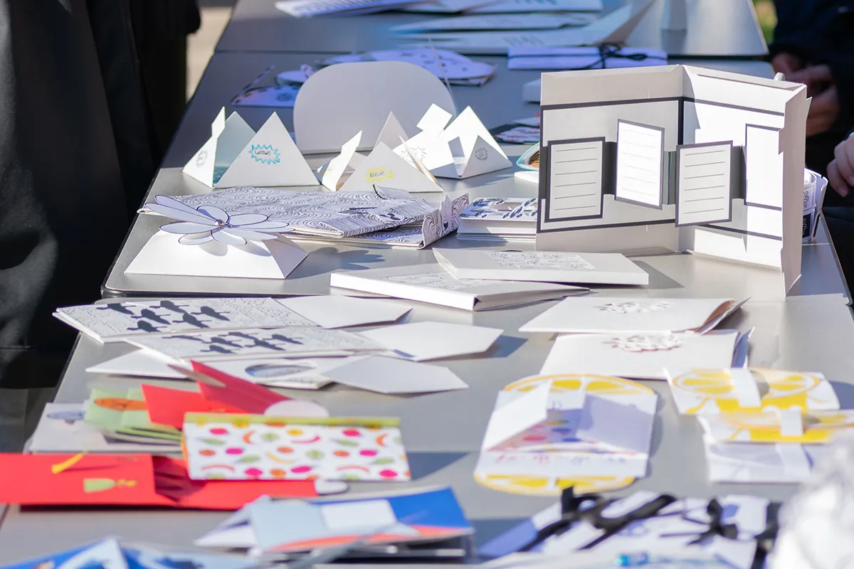 An assortment of handmade greeting cards with cutouts, patterns and illustrations, scattered about a market display table.