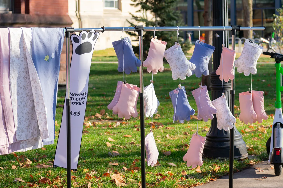 A dozen fabric, paw-shaped pillows with pink and purple colors are displayed hanging from strings.