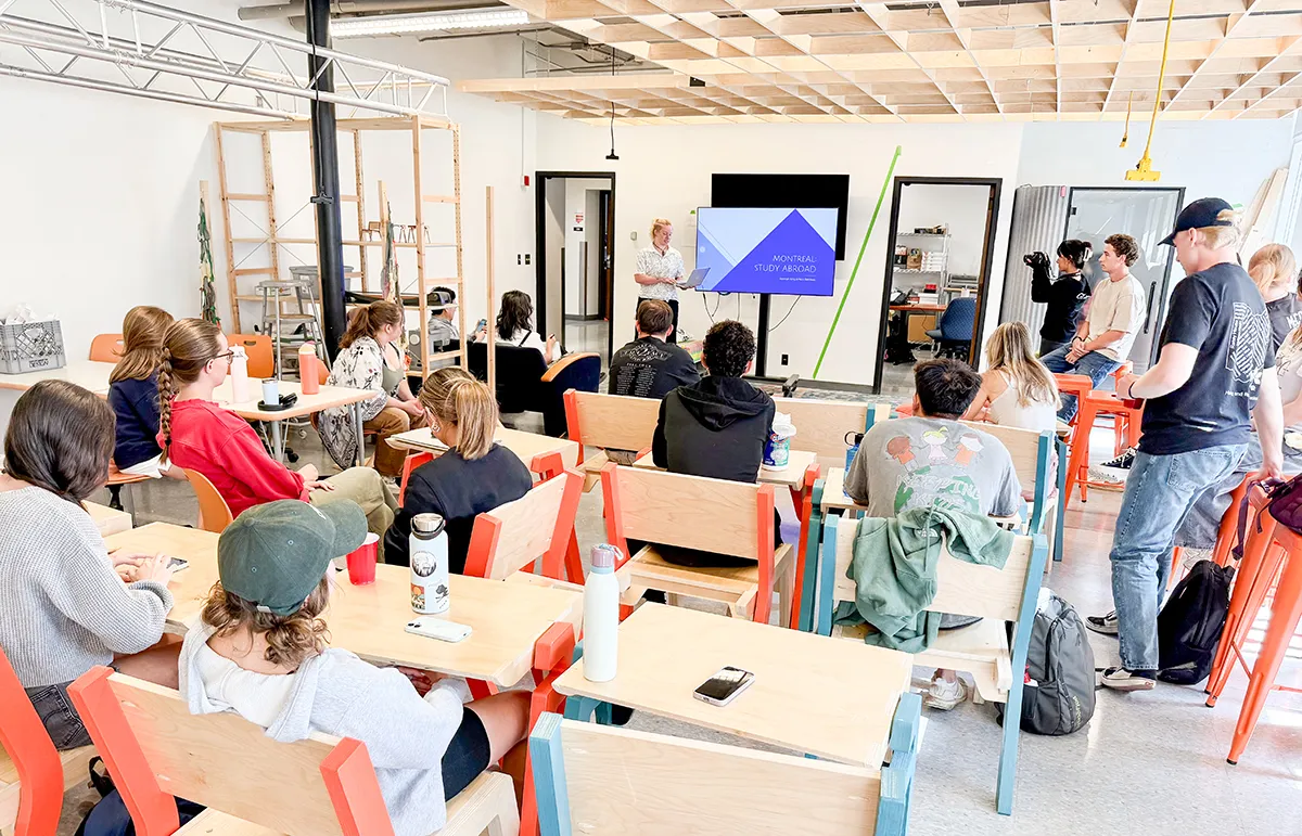 Photo of a student presenting next to a TV in front of a classroom full of students.