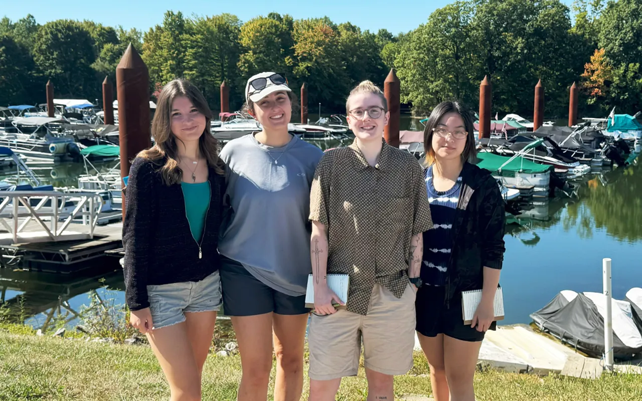 Students posing for a photo in front of a marina filled with boats.