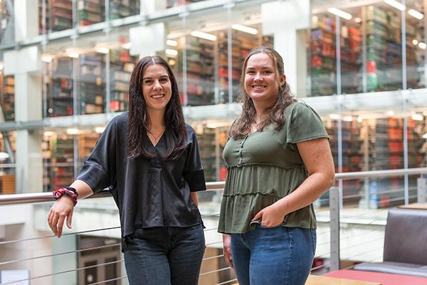 Portrait of Erika Strazinsky and Grace Gerber standing in front of bookshelves in Thompson Library.