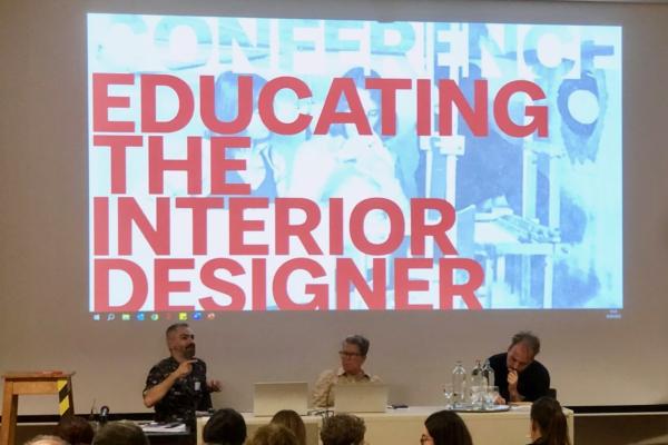 Panelist seated at a table in front of a projection that states "Educating the interior designer."