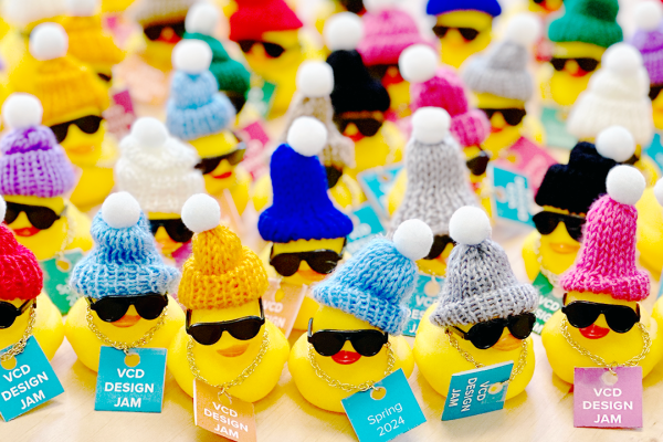 Rubber ducks wearing sun glasses and stocking caps holding signs that say "Visual Communication Design Jam 2024!"