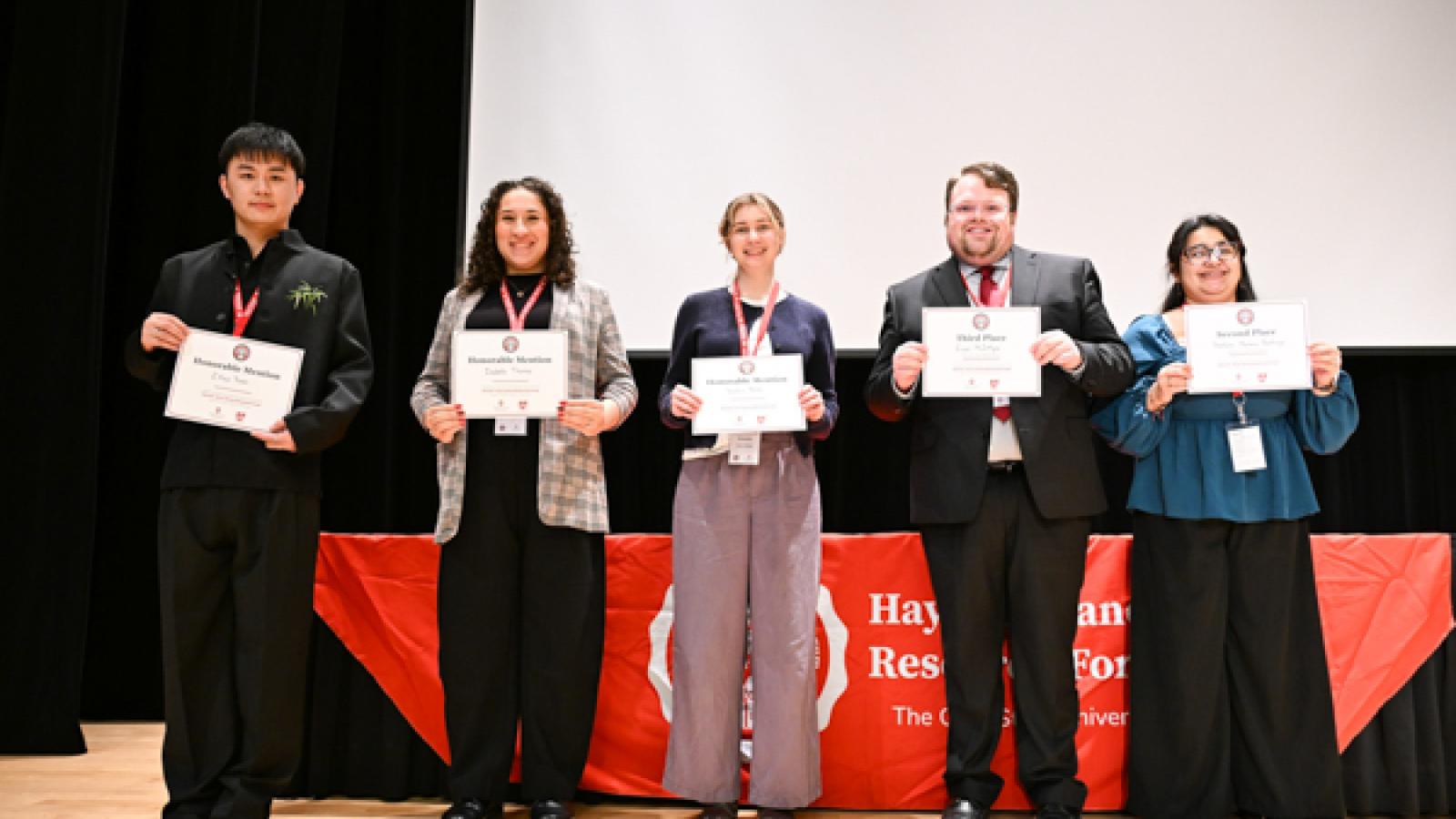 5 students stand holding award certificates