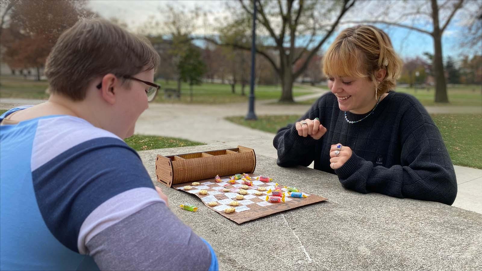 two students play checkers on a handcrafted play mat made from upcycled plastic bags