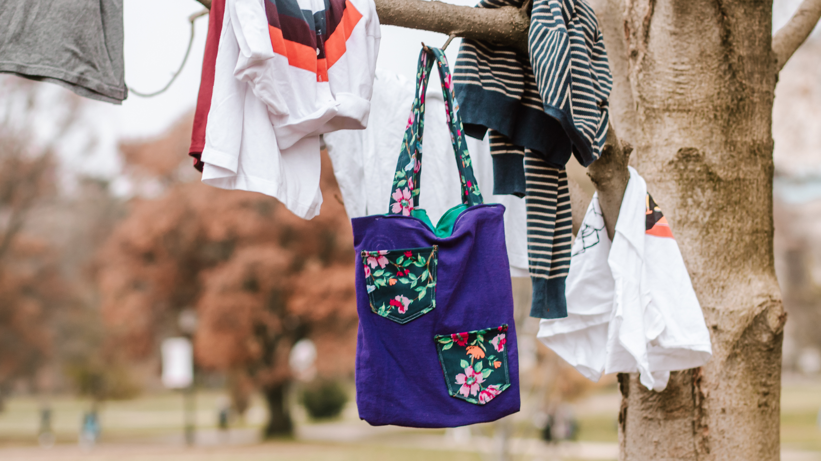 handcrafted bag pictured hanging from a tree alongside t-shirts