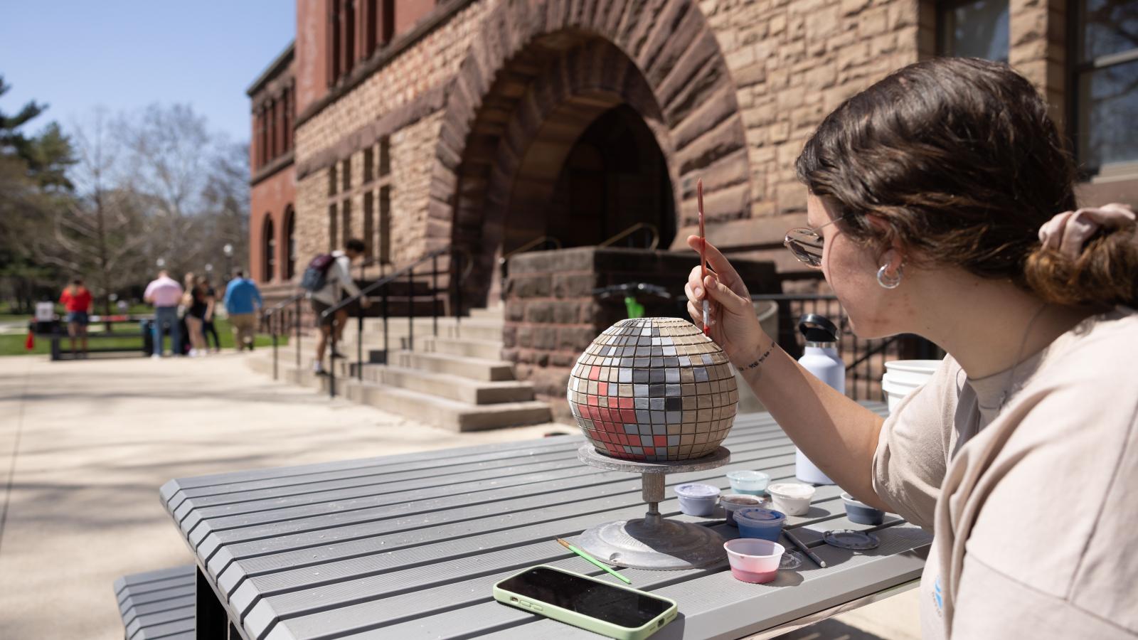 A student paints on an art project outside of Hayes Hall on a warm spring day.