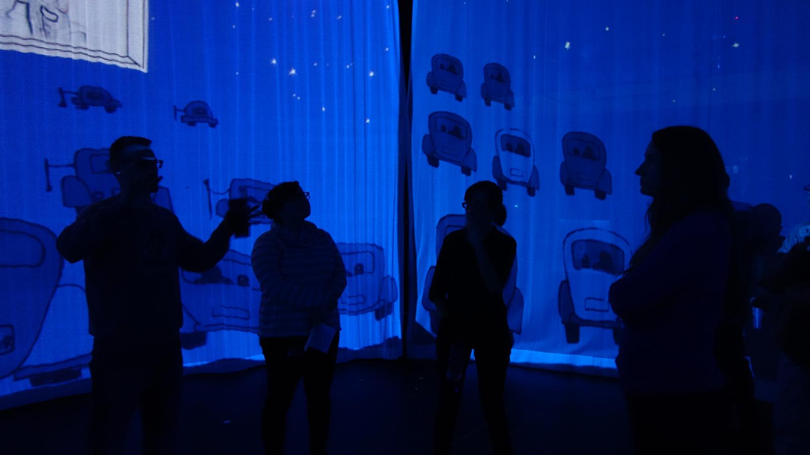 Four people in silhouette inside of a circular blue projection screen.