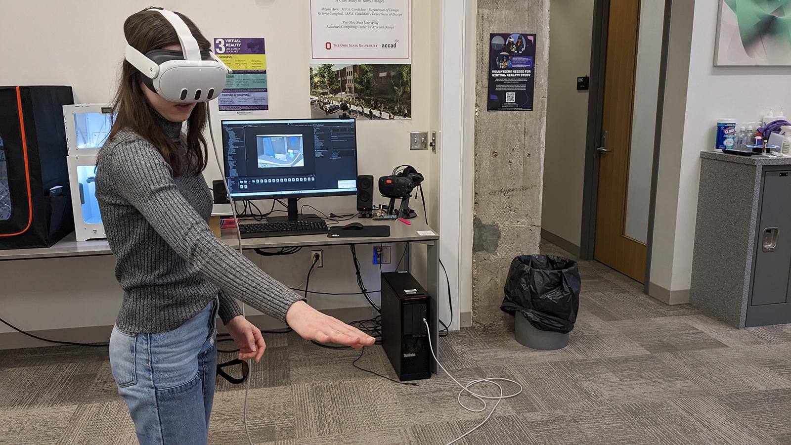 A person wearing a VR headset with their right arm extended and a screen in the background showing what the person is seeing.