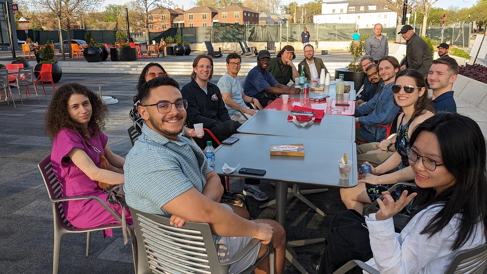 Seventeen people sitting around a long table, looking at the camera, outdoors on the OSU campus.