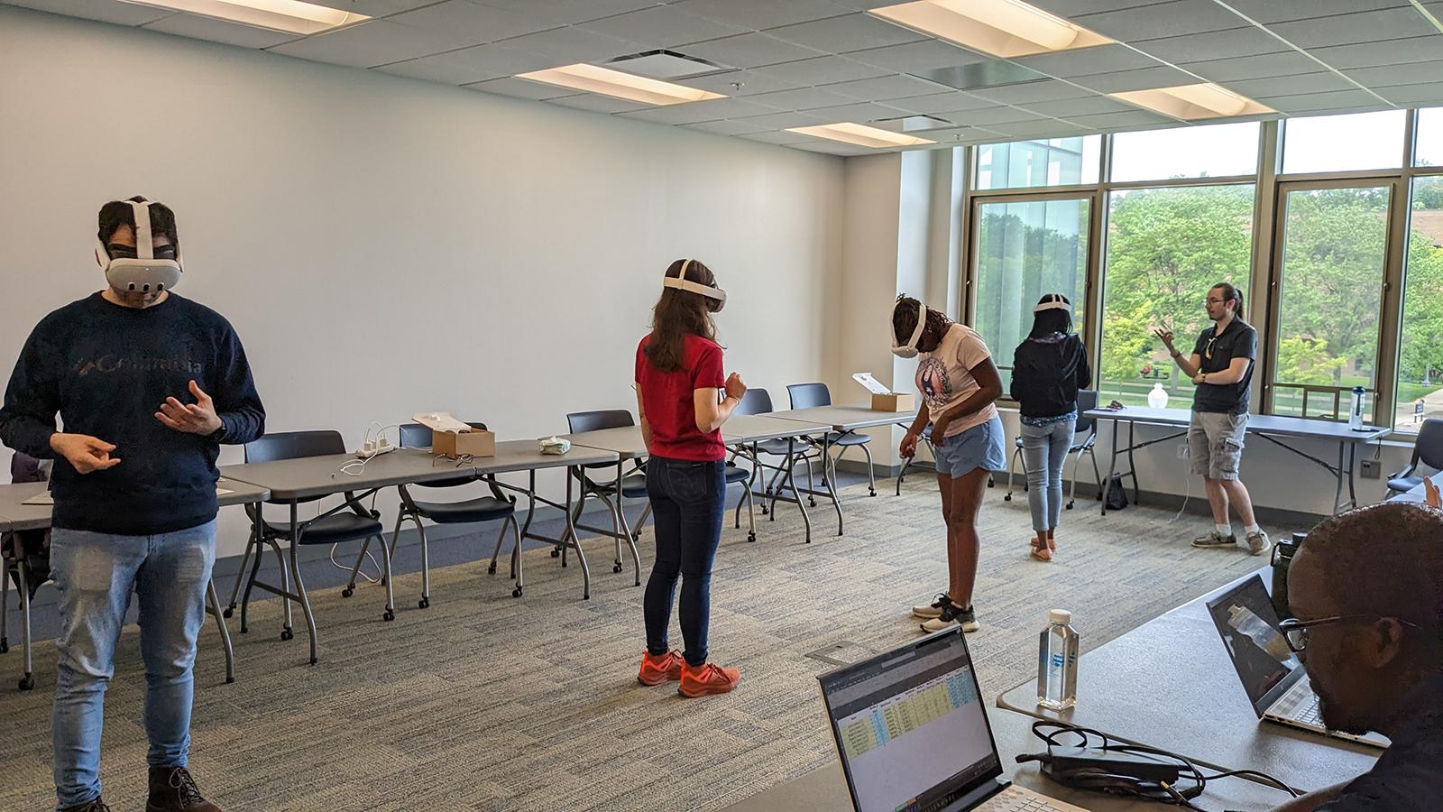 A classroom in which 4 people are wearing VR headsets and 1 person is giving instructions.