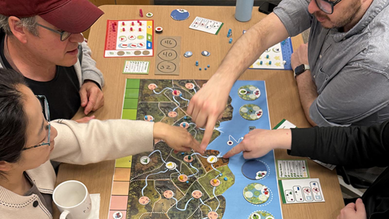 Top down view of four people sitting round a wooden table playing a board game.