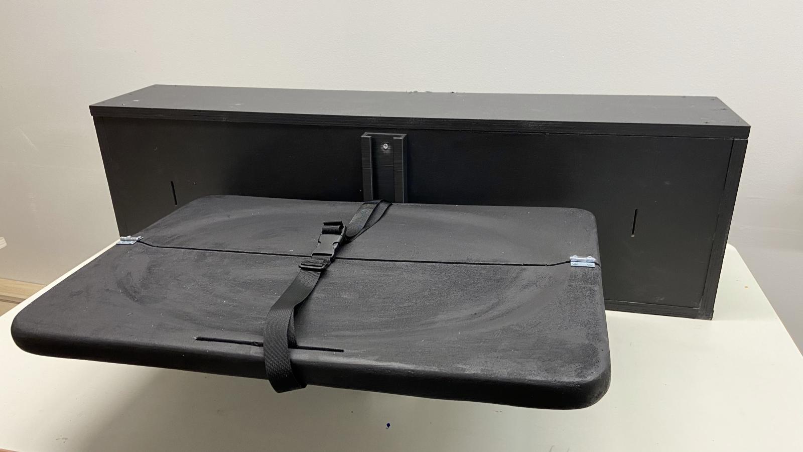 The Frunk Changing table prototype is unfolded as if you were about to change your baby. The table part is split in half long-ways, hinging so that it can fold up against the back of the frunk when not in use. The table has a buckled safety strap across the middle.
