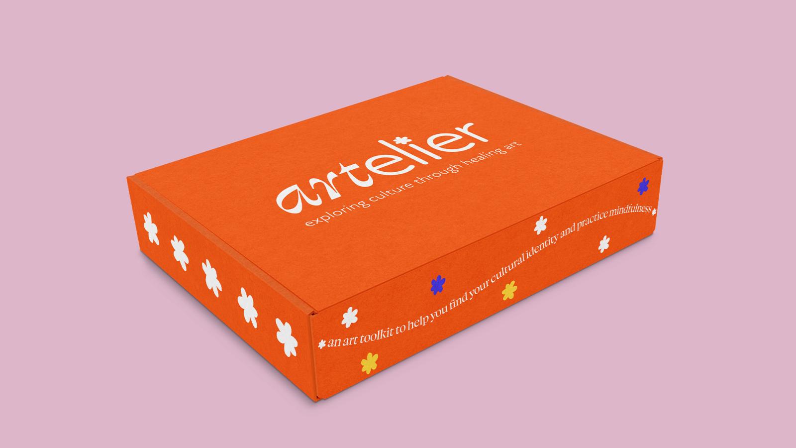 The outside packaging of the Artelier toolkit, which is a bright orange box with white text reading the name and the sentence “an art toolkit to help you find your cultural identity and practice mindfulness.”