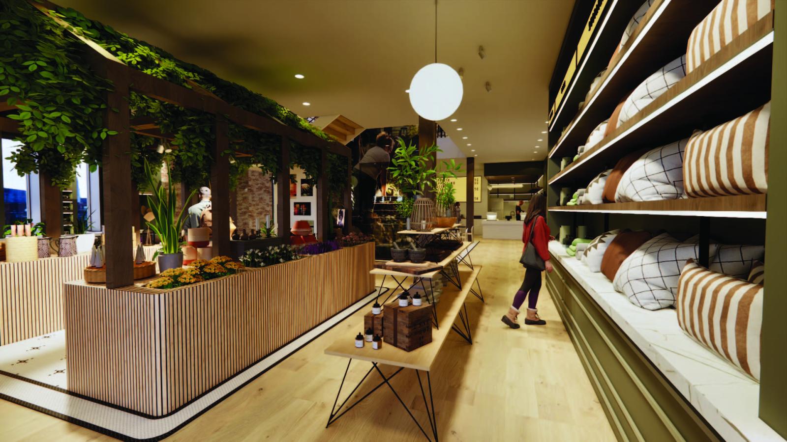 The retail space shows a walk-through display fixture with draping greenery. A long table showcases products from local creatives along with a large built in casework unit being used for more display. A mix of oak plank flooring and mosaic hexagon tiles are used for spacial definition. In the background, a slight view of the cafe is seen with a white subway tile counter.