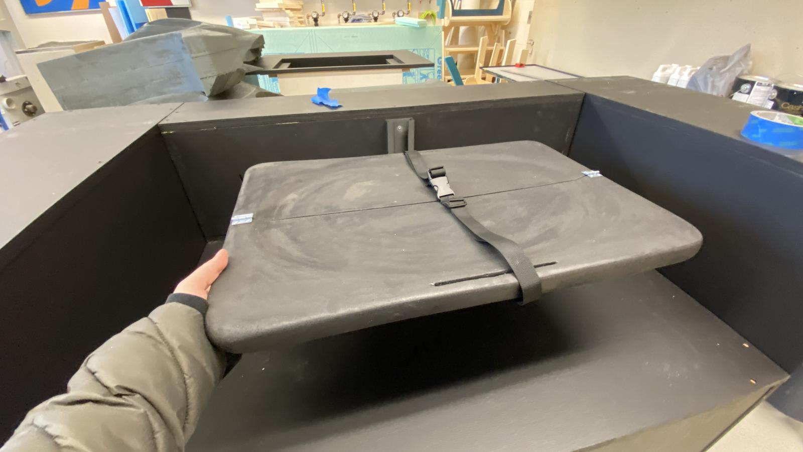 The changing table prototype is placed into the base boxes of the truck model, showing how it would proportionally fit into the space. An arm holds the bottom left corner of the table, as if the table is being unfolded and pulled out for use.