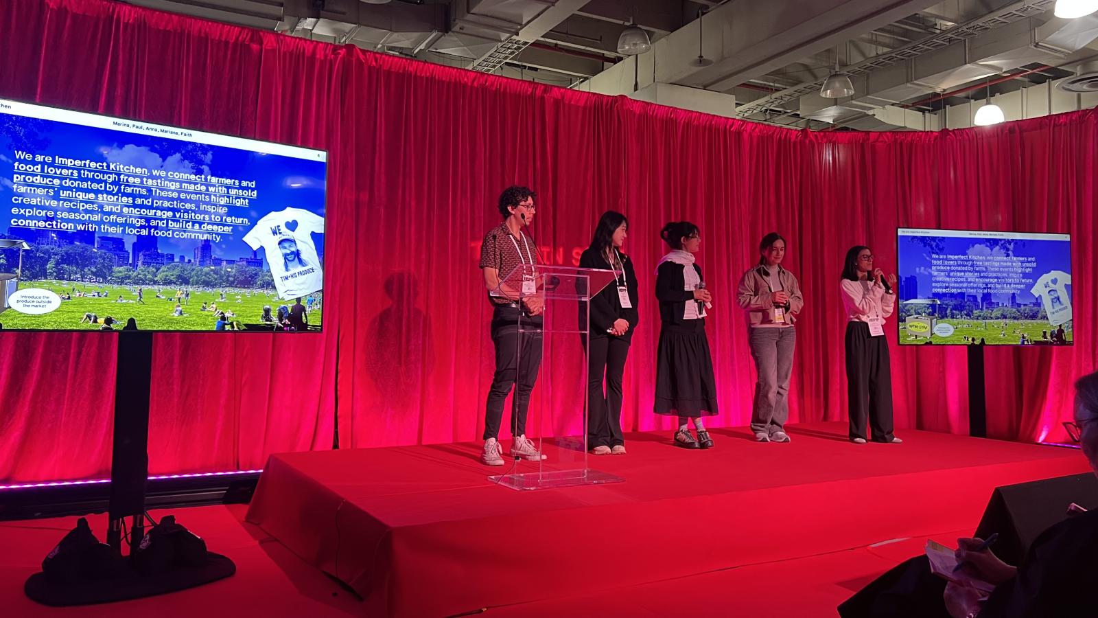 Students presenting on a stage bathed in scarlet light