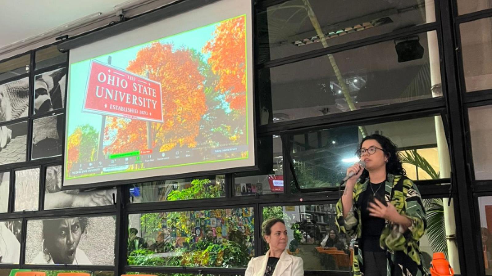 Barbara speaks with a microphone in front of a screen with the Ohio State University sign